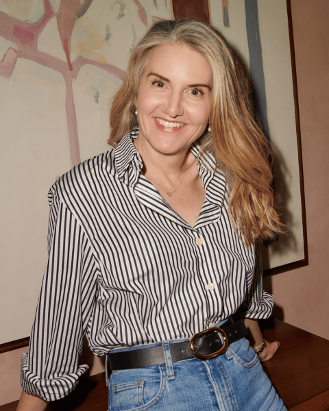Blonde woman in a buttondown blouse jeans and a belt.