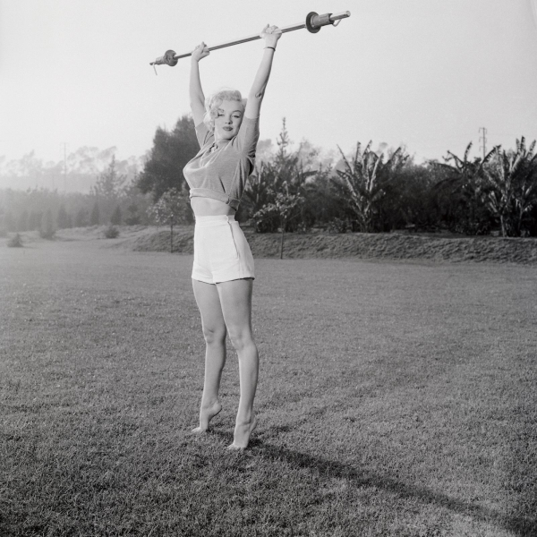 Marilyn Monroe reaching for the sky on tiptoe holding a light barbell.